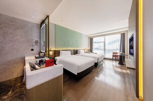 A hotel room with a large bed, a desk with a computer, a mirror, and a view of the city skyline through the window.