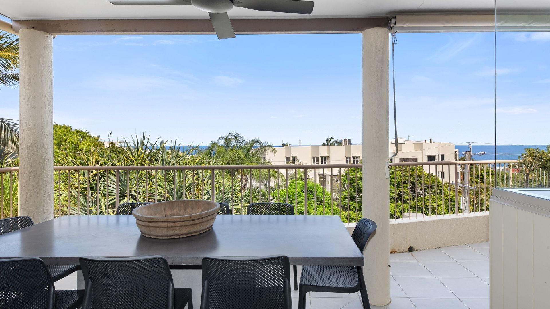 A covered outdoor dining area with a table and chairs, a large bowl, and a view of the sea and buildings.