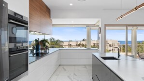 A modern kitchen with a large island, a built-in oven, and a view of the city and sea.