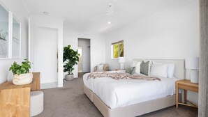 A modern bedroom with a large bed, bedside tables, a floor lamp, and a potted plant.