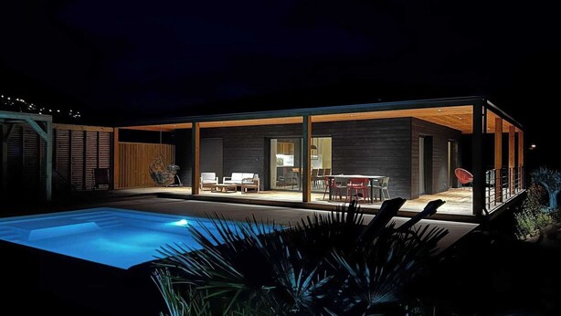 Une maison moderne dotée d’une piscine, de grandes portes vitrées et d’un espace patio.