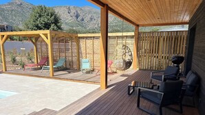 Une terrasse couverte avec un plancher en bois, du mobilier d’extérieur et une vue sur les montagnes.