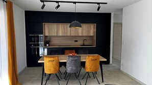 Une cuisine moderne avec des meubles en bois, un luminaire suspendu noir et une table à manger avec quatre chaises.
