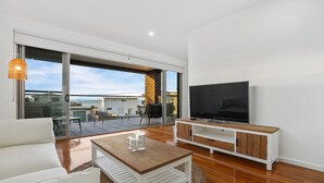 A modern living room with a sofa, coffee table, TV, and a sliding glass door leading to an outdoor patio.