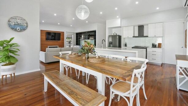 A modern kitchen with white cabinetry, a wooden dining table, and a bench.
