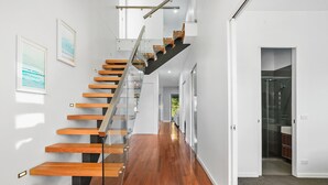A modern interior with a wooden staircase, a hallway, and a bathroom visible through an open door.