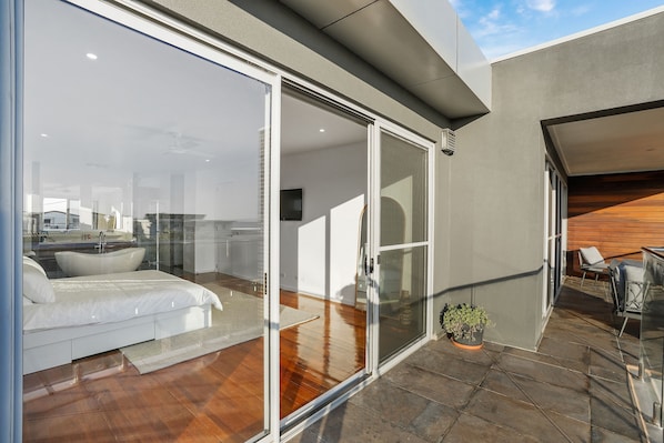 A modern bedroom with a glass door leading to a balcony, a wooden ceiling, and a potted plant. - Spacious beach house - 2 min walk to the beach & 1.6km from town. (Portarlington)
