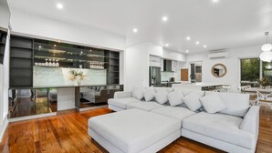 A modern living room with a sectional sofa, wooden flooring, built-in shelving, and a kitchen area in the background.