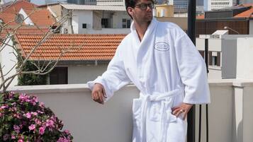 A person in a white bathrobe standing on a rooftop with a cityscape in the background.
