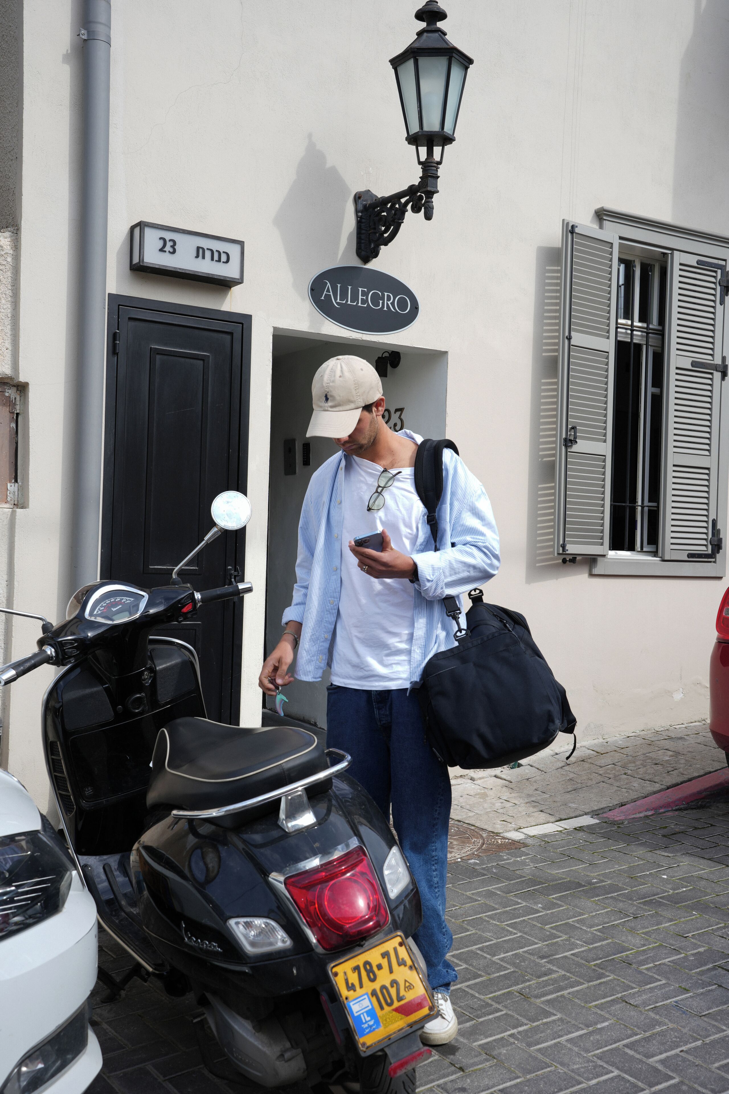 A man standing next to a scooter with a license plate, a building entrance, and a street lamp.