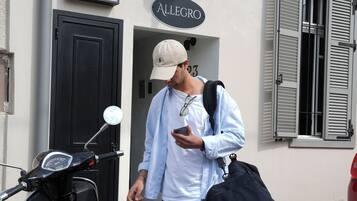 A man standing next to a scooter with a license plate, a building entrance, and a street lamp.