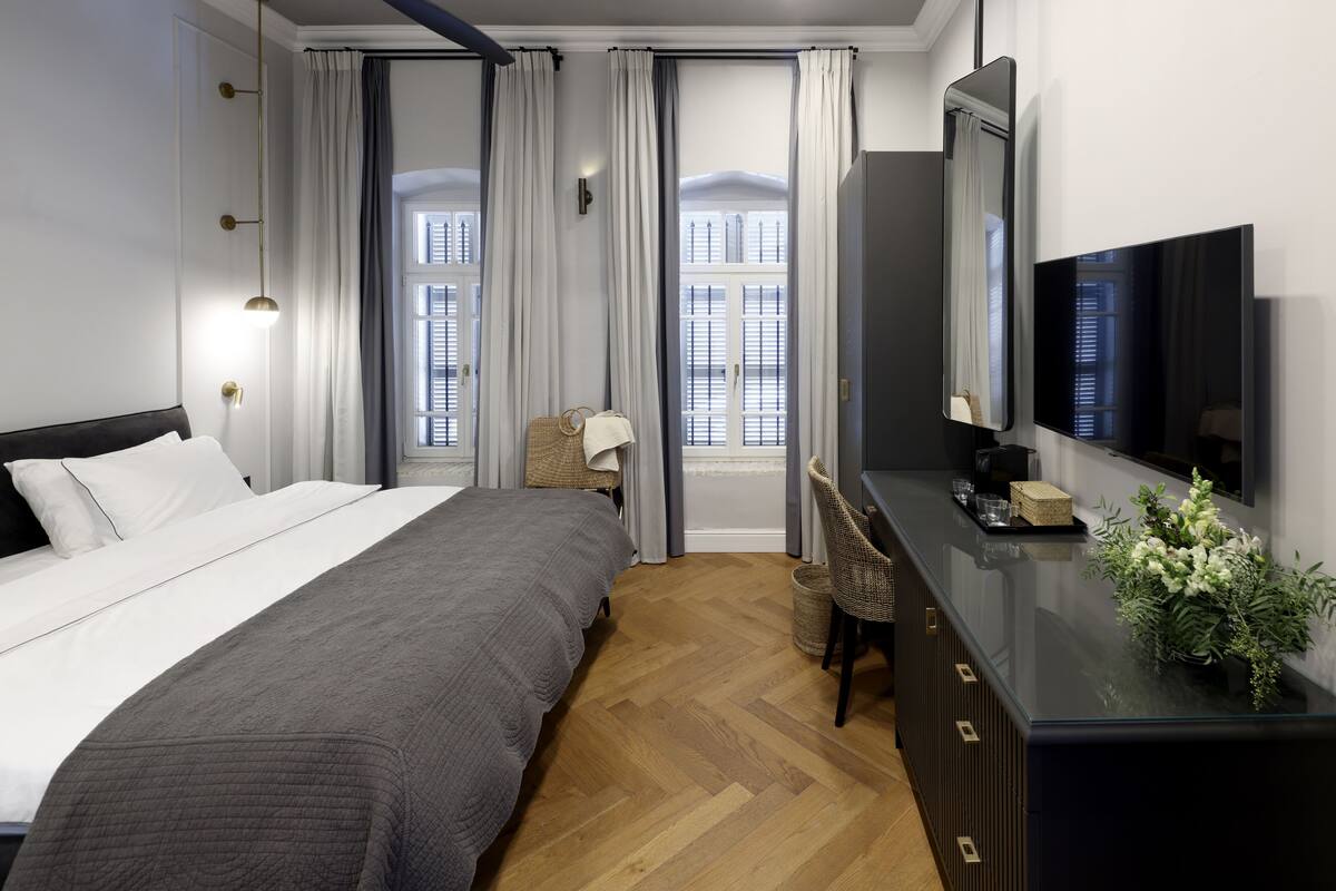 Ein modernes Hotelzimmer mit einem großen Bett, einem Schreibtisch, einem Flachbildfernseher und Blick durch große Fenster nach draußen.