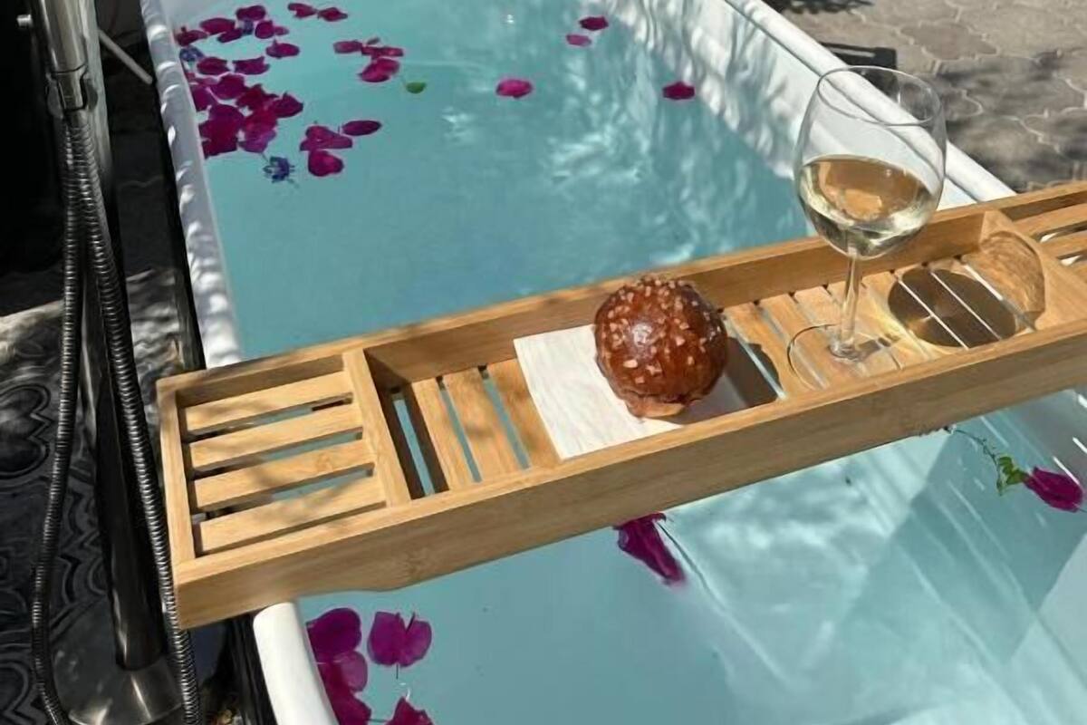 Ein Whirlpool mit darin treibenden Rosenblüten, ein Glas Weißwein und ein Holztablett mit einem Donut.
