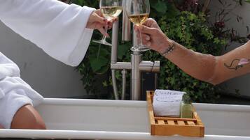 Una persona sostiene una copa de vino blanco, un ramo de rosas rosadas y un croissant sobre una mesa de madera.