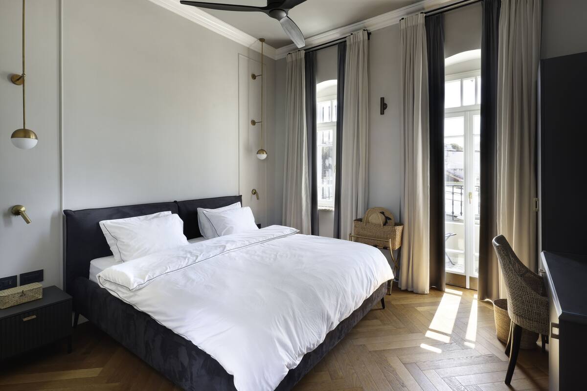 Ein modernes Schlafzimmer mit einem großen Bett, einem Deckenventilator und Blick ins Freie durch große Fenster.