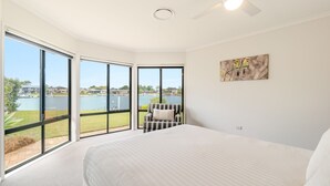 Quarto com cama grande, uma cadeira e vista para um lago e edifícios.