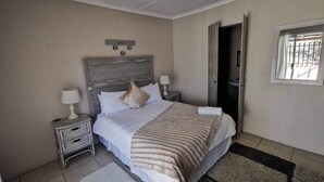 Un dormitorio con cama, dos mesitas de noche, una ventana y una puerta.