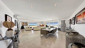 A spacious living area with a large window overlooking a scenic view, a dining area with a glass table, and a decorative vase. - ★Luxury Penthouse w/Stunning Sea Views, Walk Beach (Albufeira)