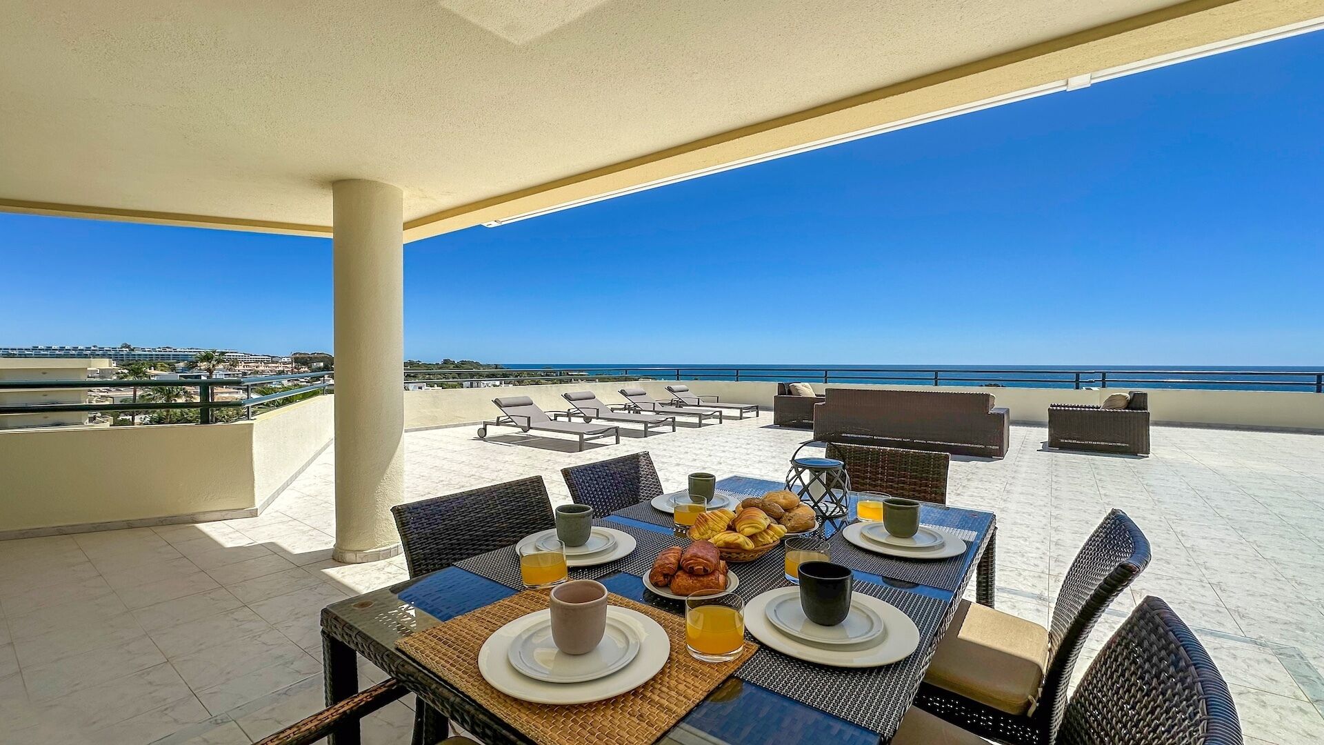 A terrace with a table set for breakfast, overlooking a beach and ocean.