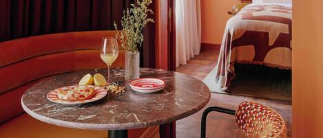 A dining area with a round table, a plate of food, a glass of drink, and a vase with flowers.