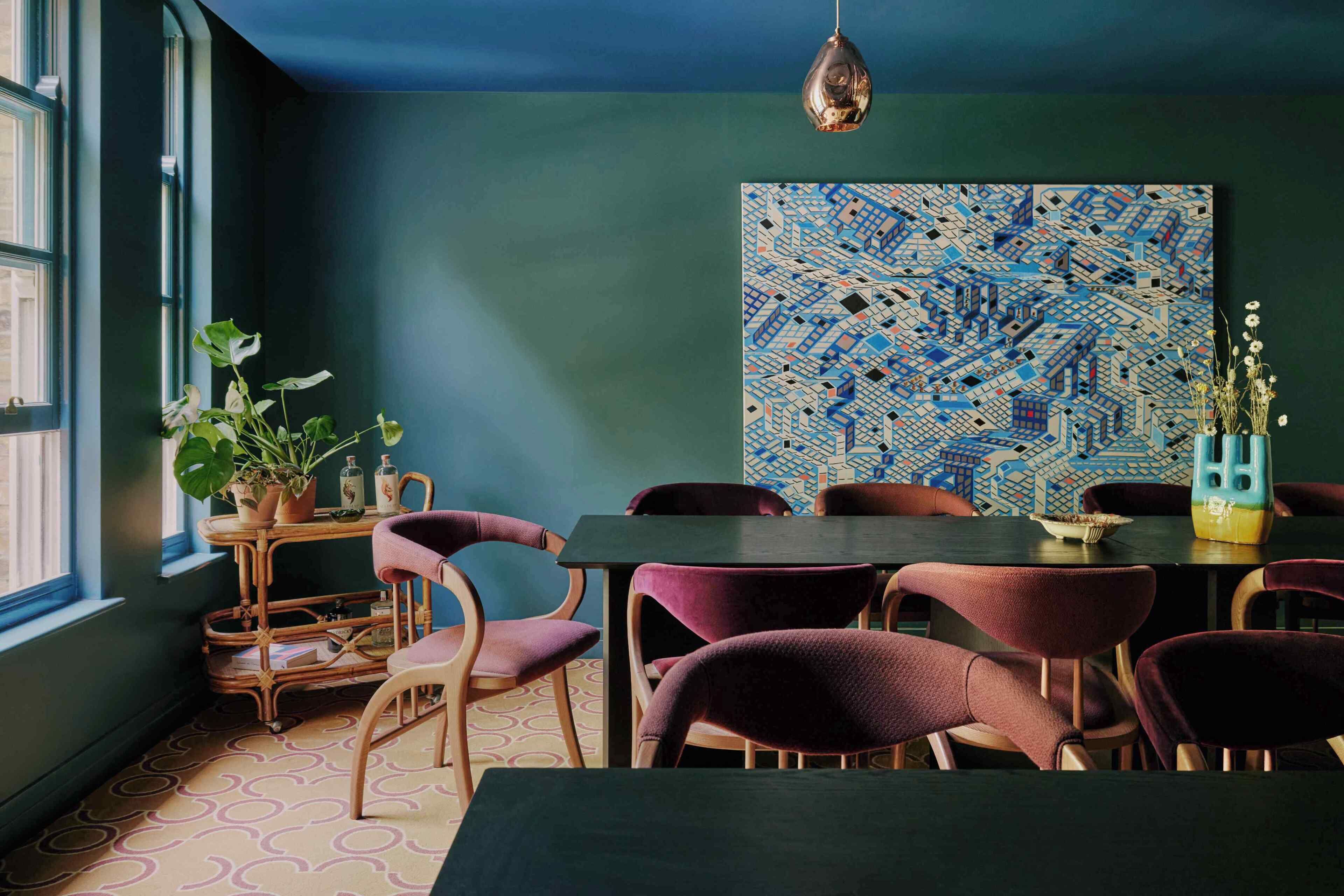 A dining area with a table, chairs, a hanging light fixture, and a large abstract painting on the wall.
