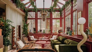 A conservatory with wicker furniture, a green sofa, and potted plants. - Ember Locke Kensington (London)