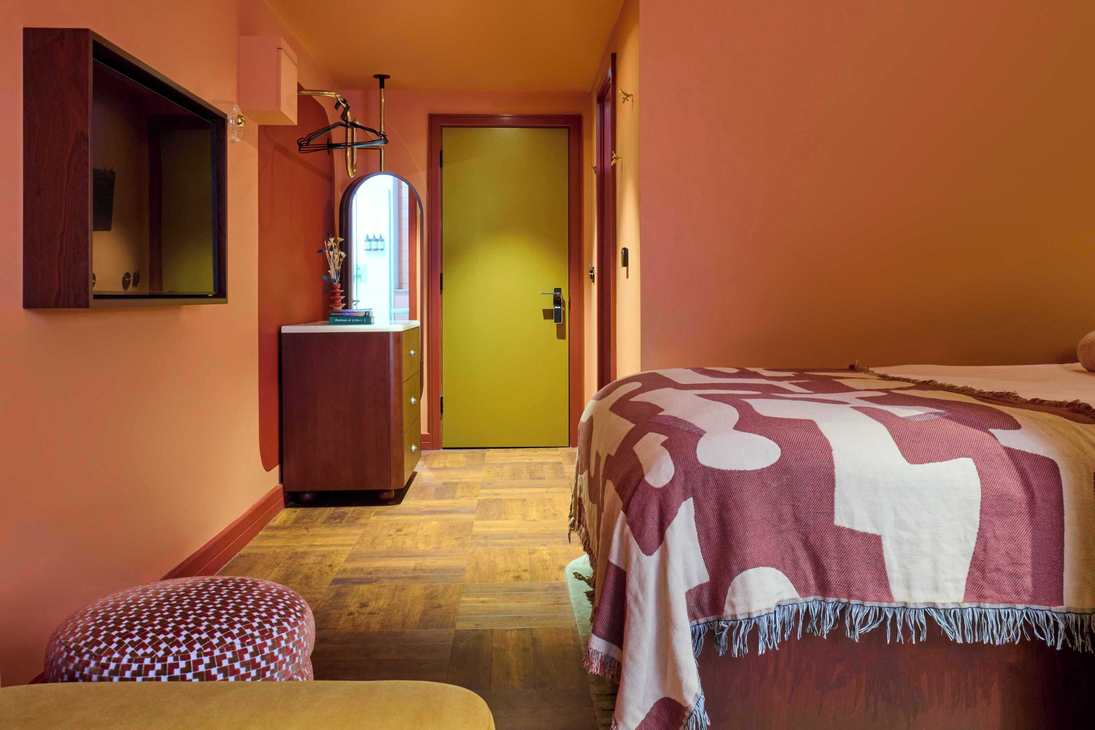 A hotel room with a bed, a wooden dresser, a mirror, and a door.