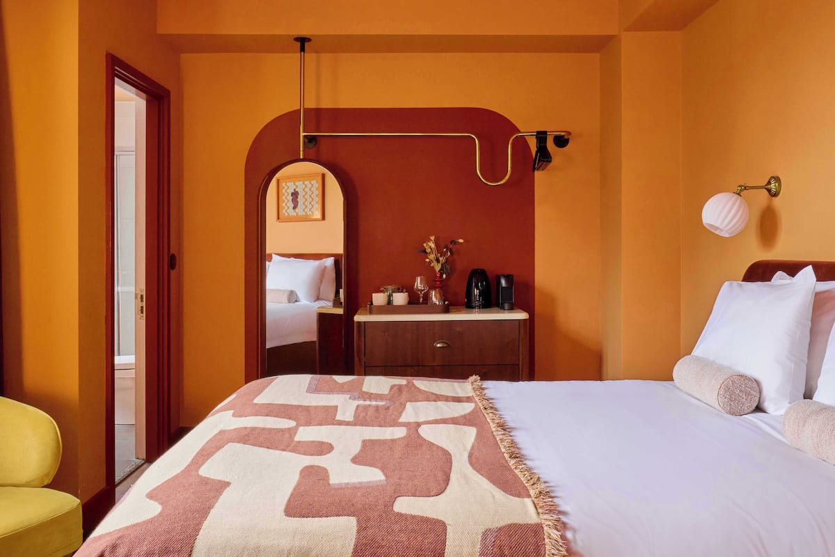 A hotel room with a bed, a bedside table, a mirror, a lamp, and a chair.