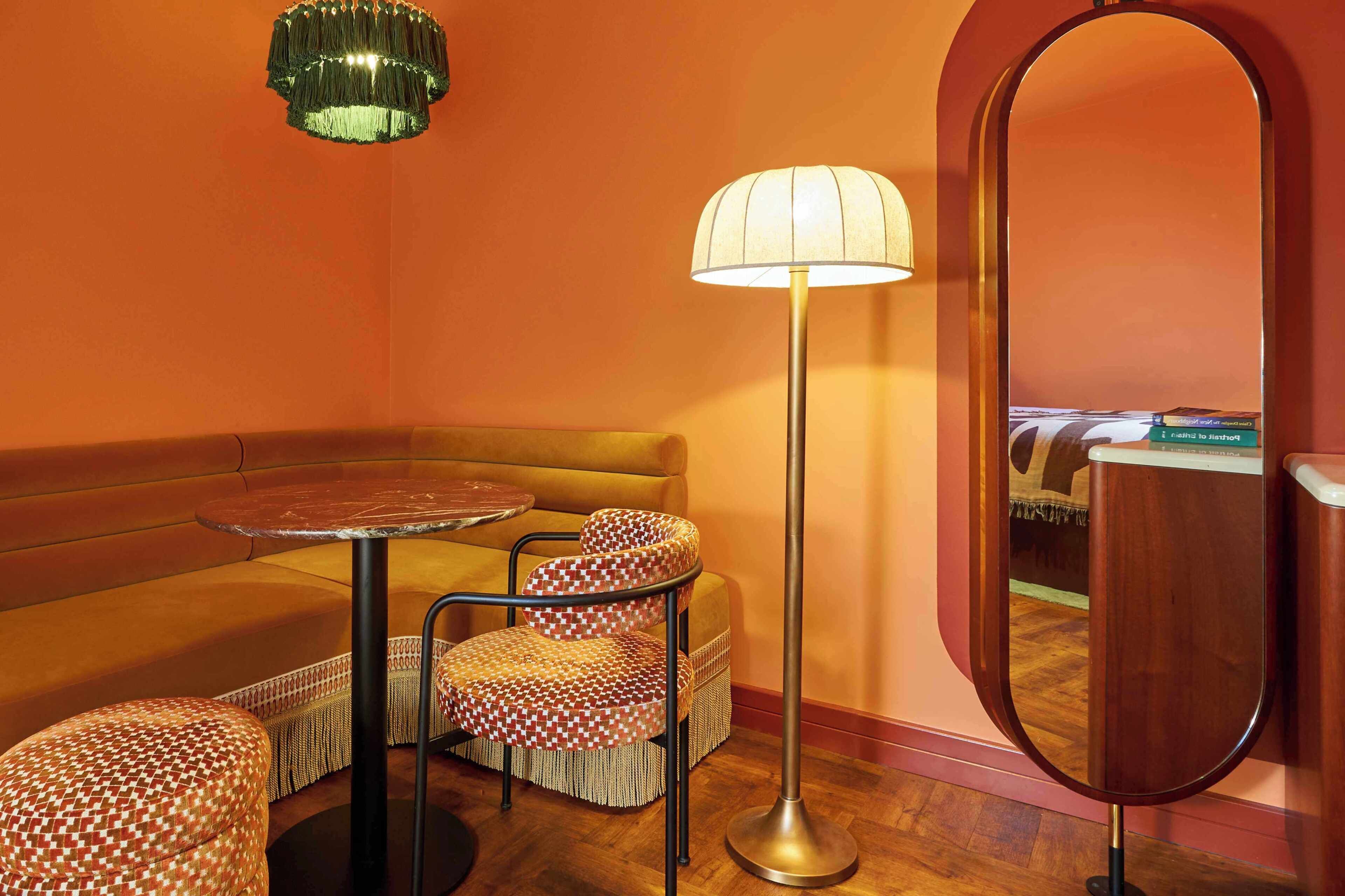 A room with a round table, a sofa, patterned chairs, a floor lamp, and a mirror.