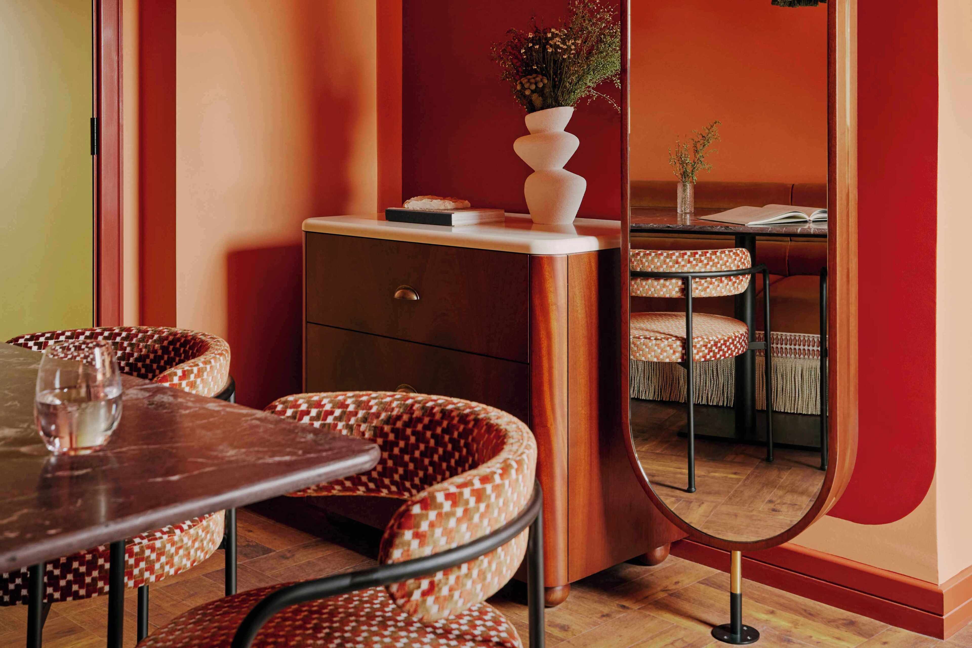 Un coin repas avec une table en bois, des chaises à motifs, un meuble orné d’un vase et un miroir qui reflète la pièce.