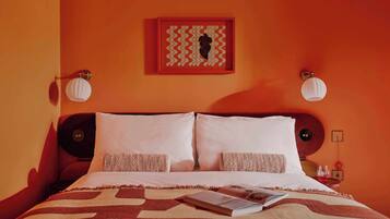A hotel room with a bed, two bedside tables, a nightstand, a framed artwork above the bed, and a wall-mounted light fixture.