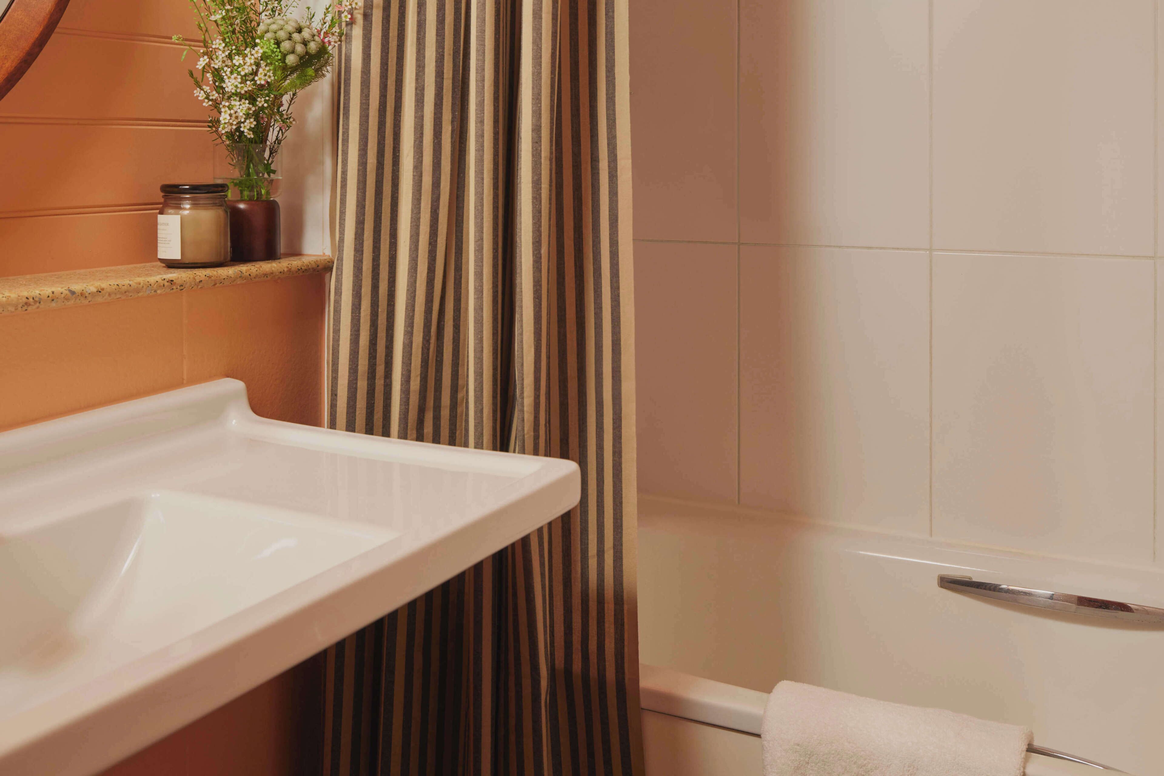 Un baño con un lavamanos blanco, una cortina de ducha a rayas y un perchero.