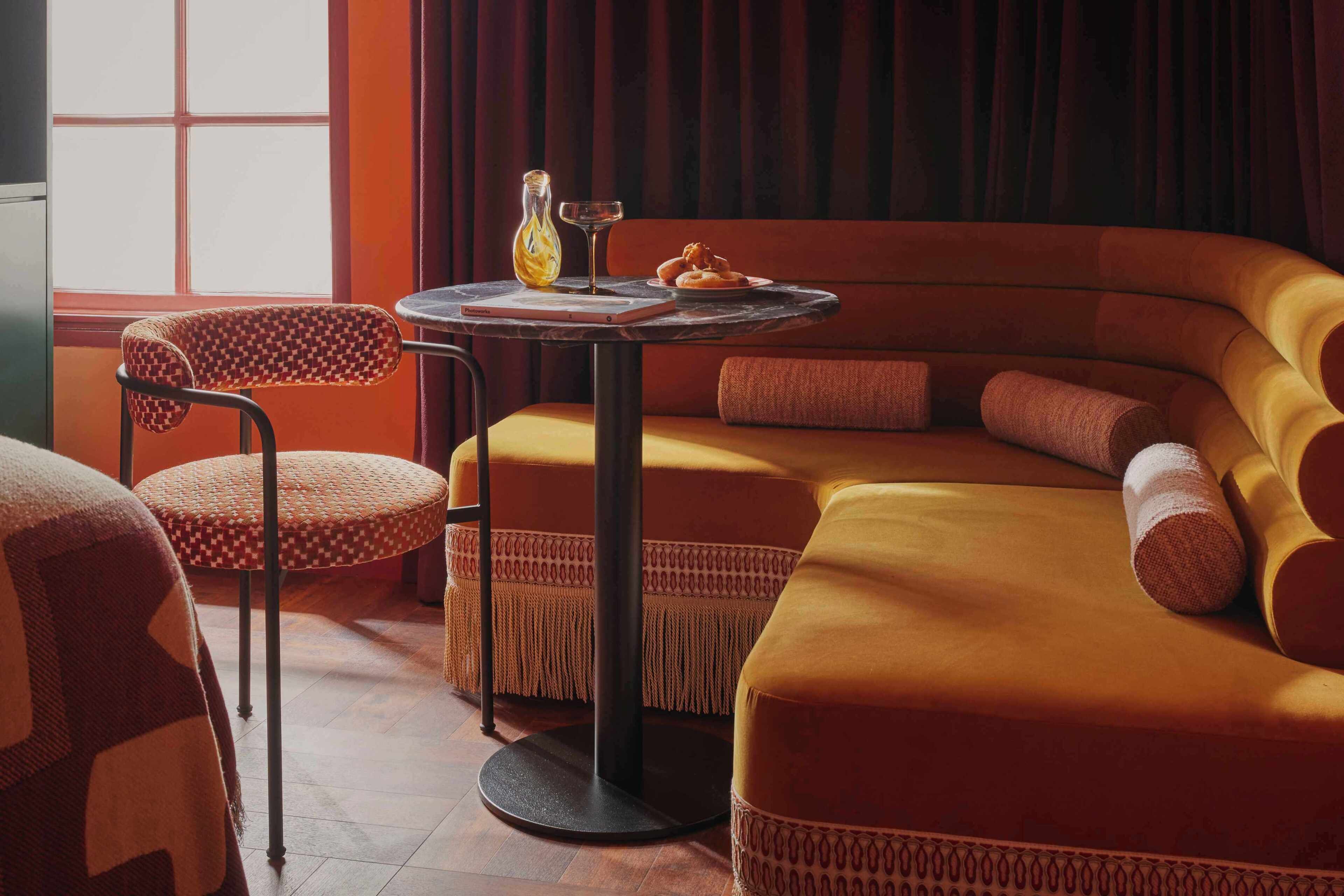 Une pièce chaleureuse avec un canapé incurvé, une table ronde sur laquelle se trouvent une bouteille et un verre, et un fauteuil à motifs.