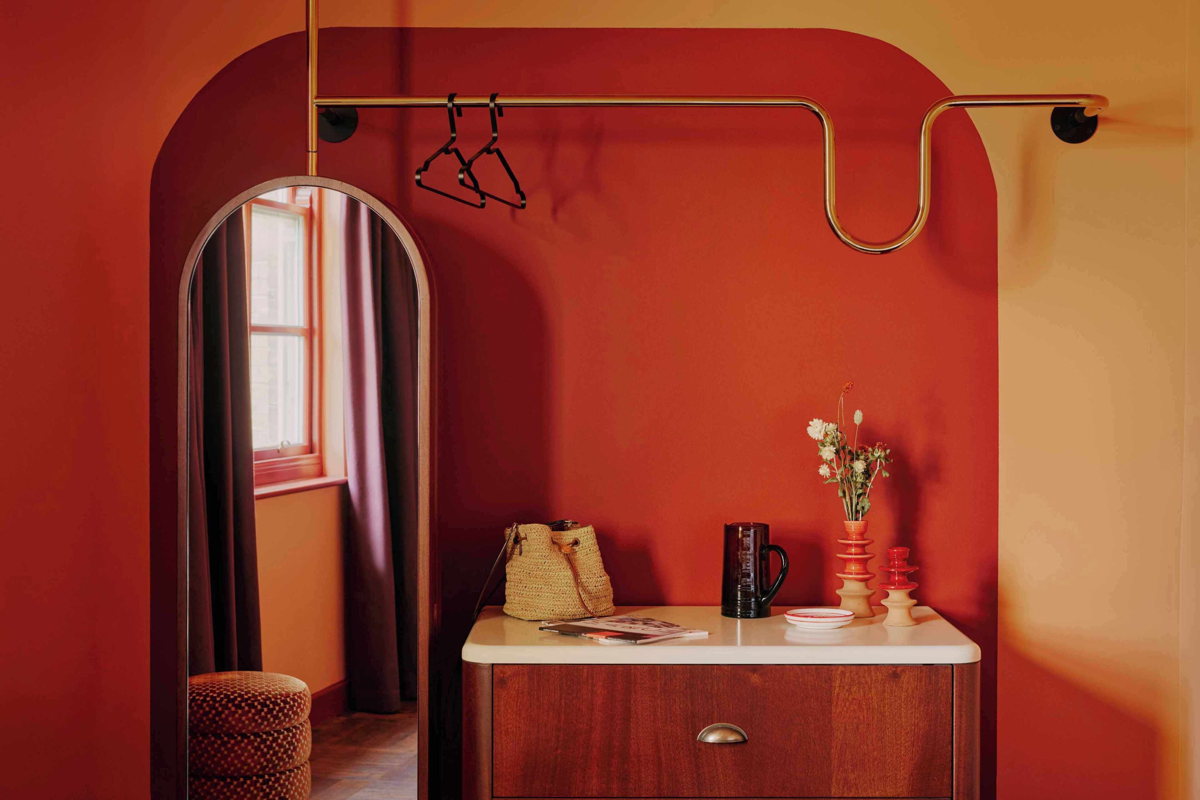 Une pièce comprenant un meuble en bois, un porte-manteau suspendu, un sac en tissu tressé, une tasse à café et un vase avec des fleurs.