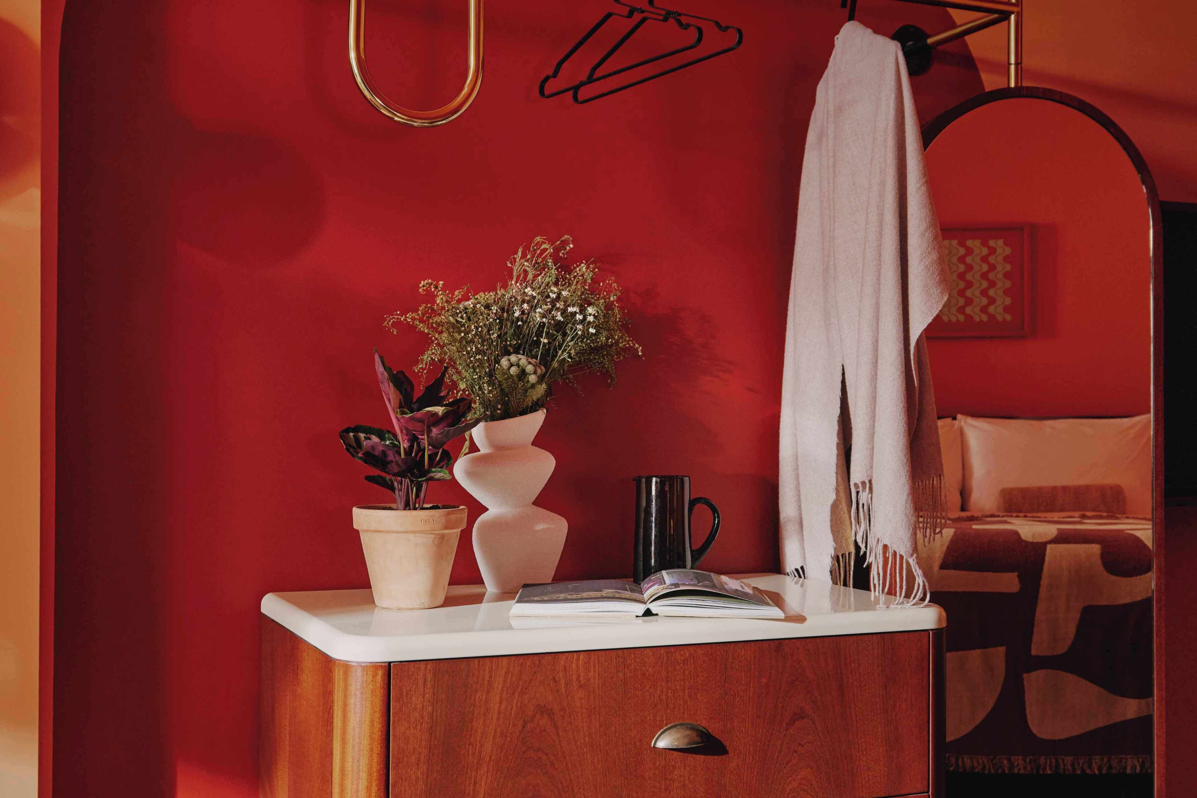 A wooden cabinet with a white countertop, a vase with flowers, a black mug, and a book.