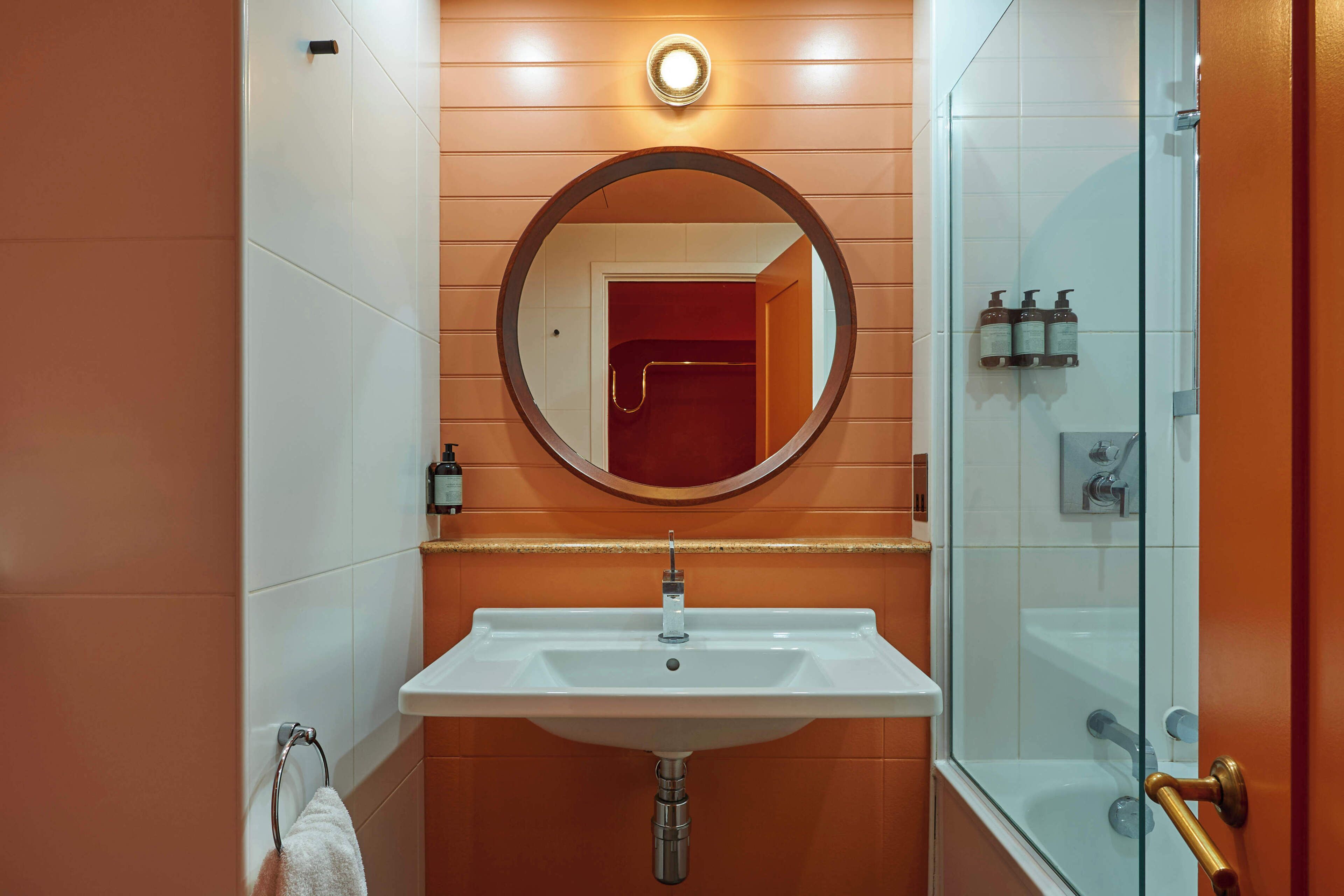 A bathroom with a white sink, a round mirror, and a glass shower enclosure.