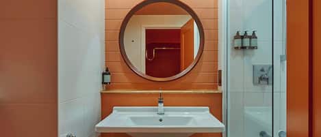 Baño con lavamanos blanco, espejo redondo y cabina de ducha de vidrio.