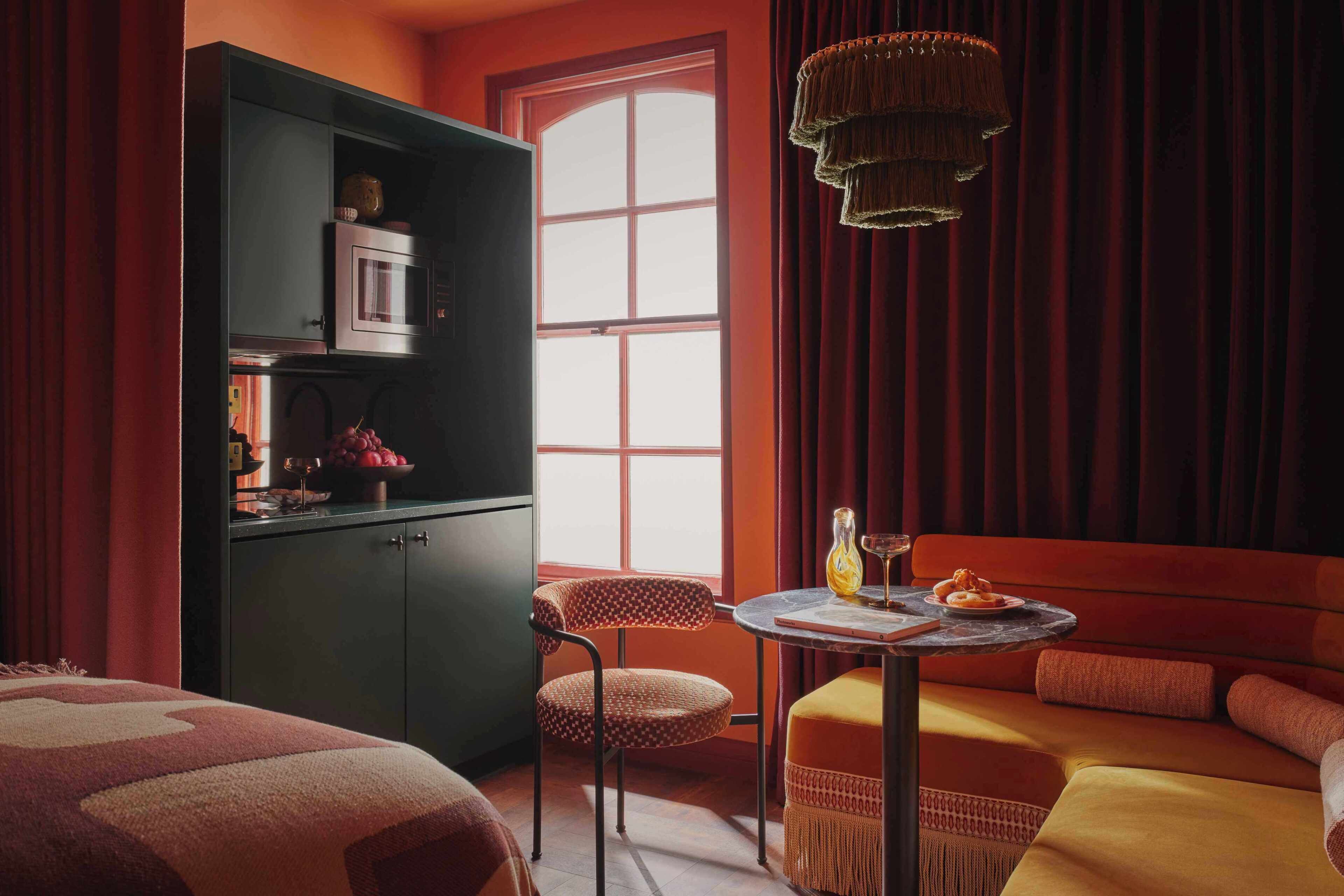 A room with a bed, a dining table with a vase and a plate, a microwave, a cabinet, and a window with curtains.