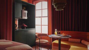 A room with a bed, a dining table with a vase and a plate, a microwave, a cabinet, and a window with curtains.