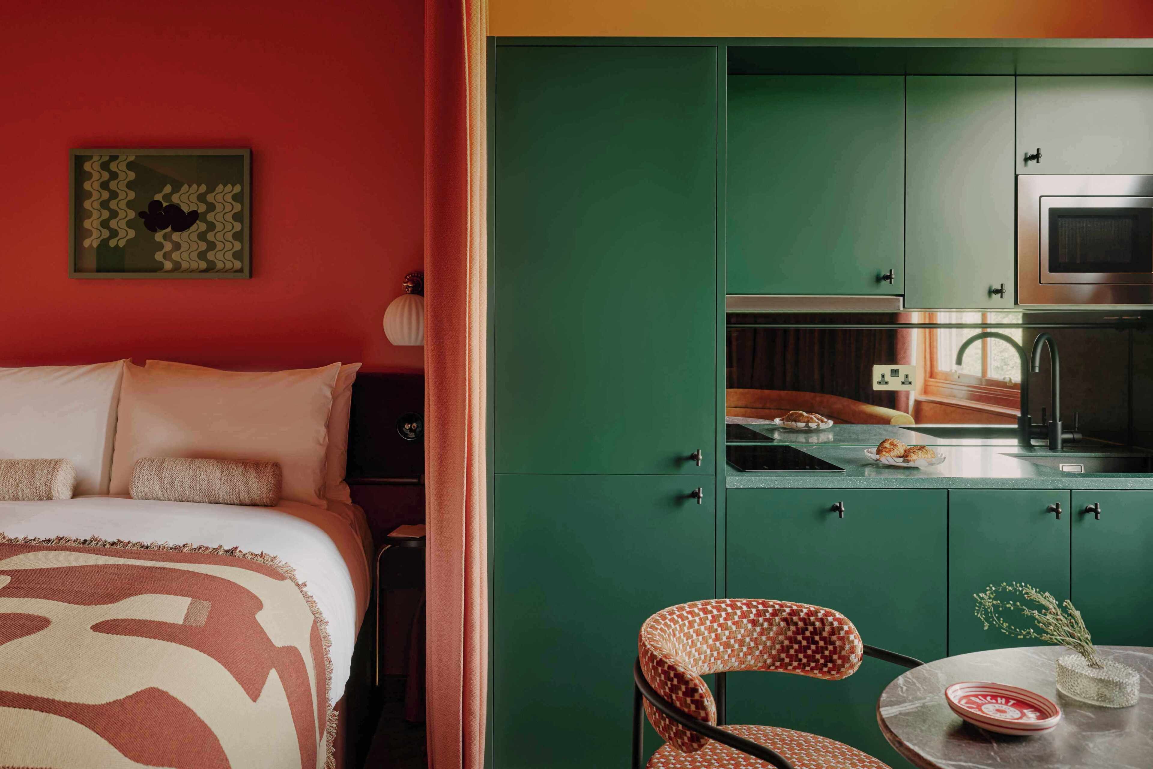 A room with a bed, a green cabinet with a microwave, and a small table with a vase.