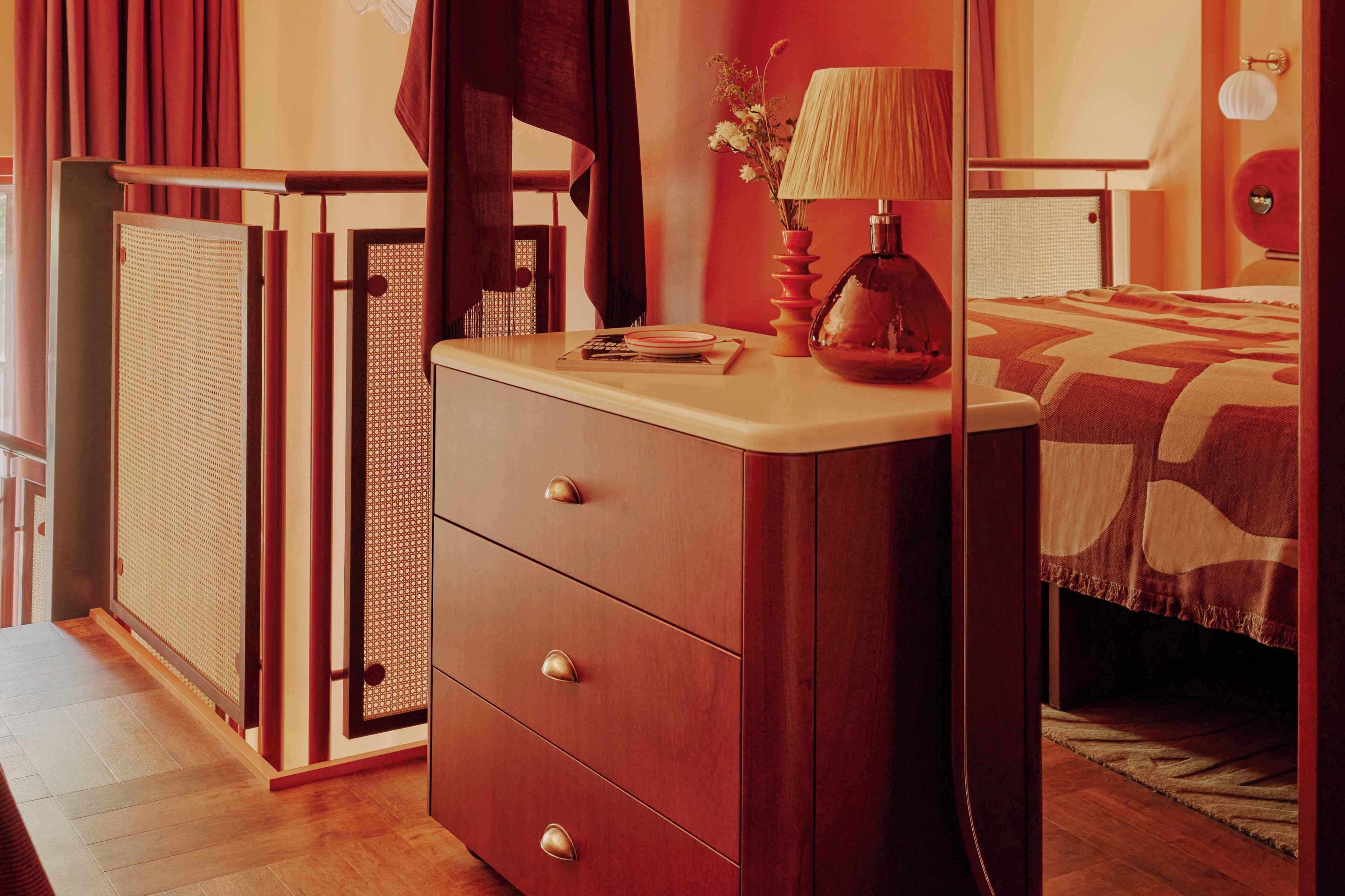A bedroom with a bed, a dresser, a lamp, and a window with curtains.
