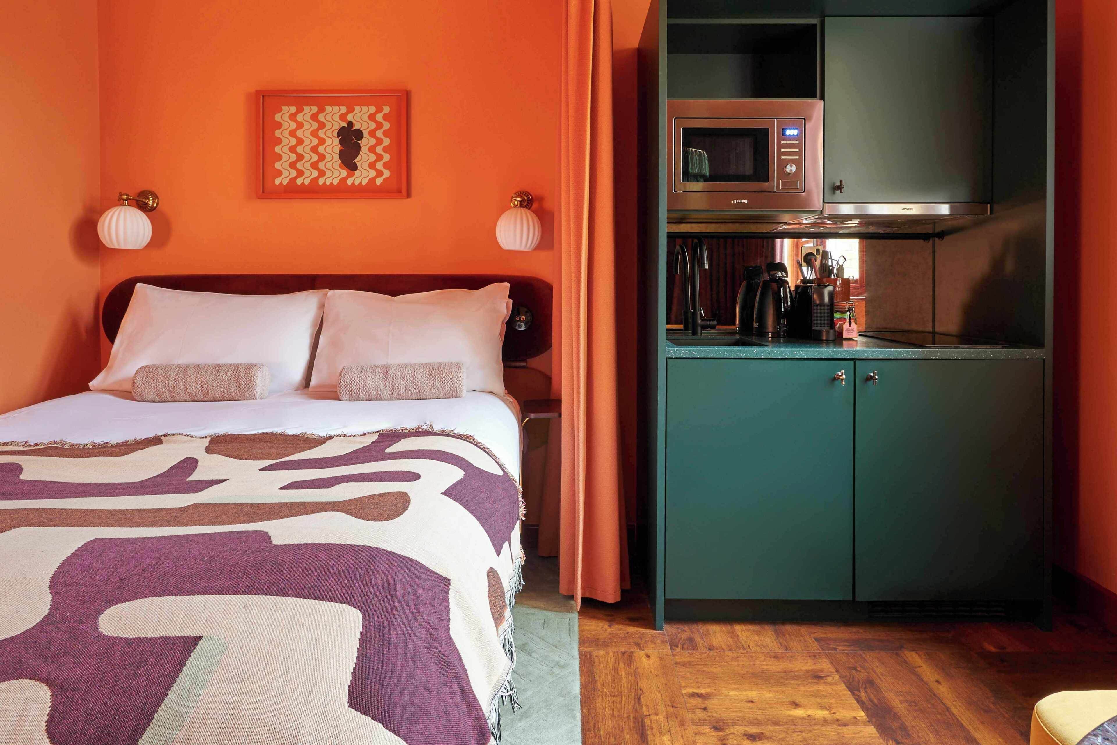 Una camera da letto con un letto, un comodino, una TV a muro e un angolo cottura con forno a microonde.