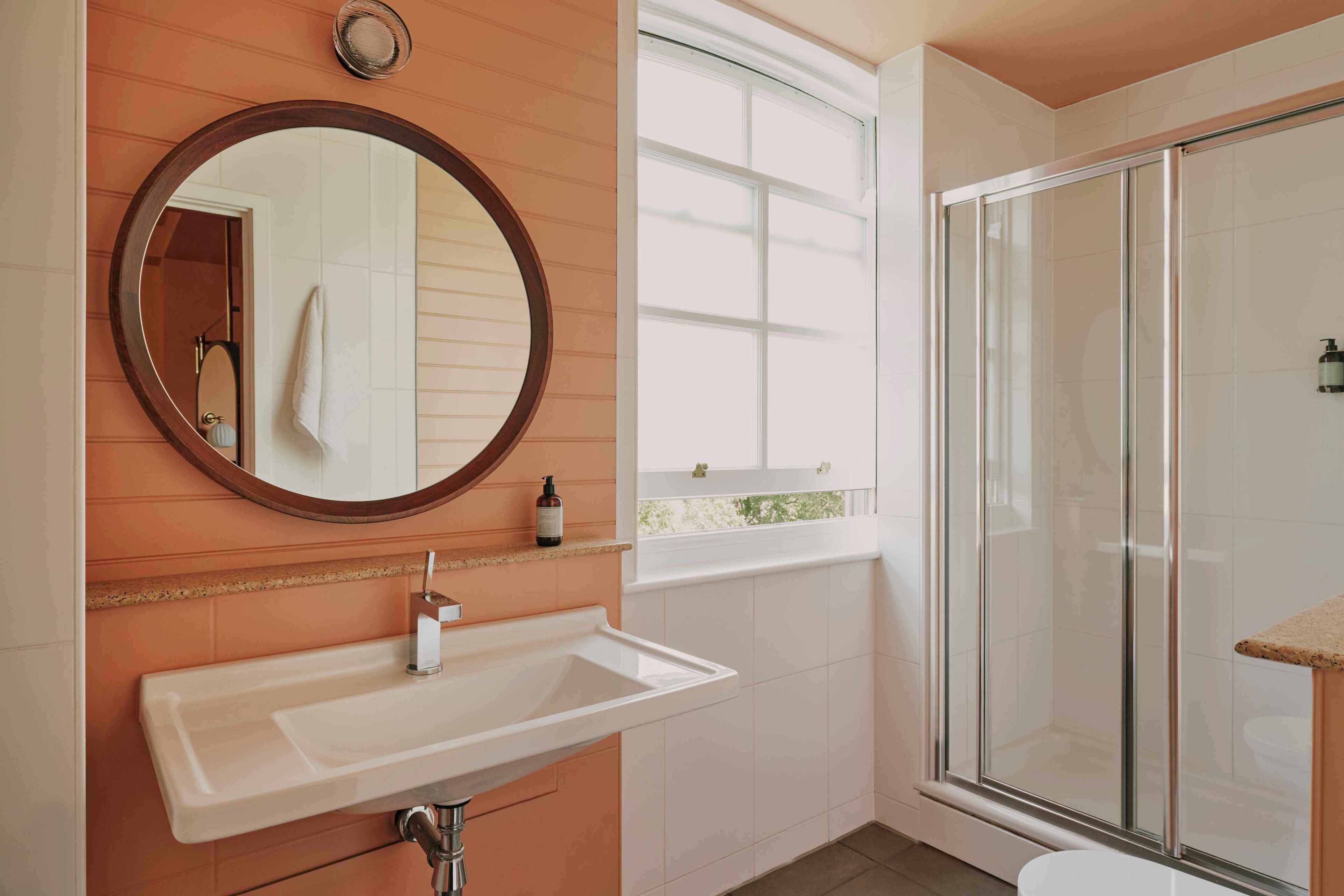 Ein Badezimmer mit Waschbecken, Spiegel, Fenster und Duschkabine.