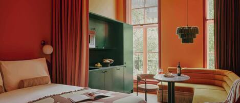 A hotel room with a bed, a green cabinet, a sofa, a small table, and a window with curtains.