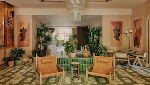 A spacious lobby with a chandelier, seating area, potted plants, and a view to the outside. - Ember Locke Kensington (London)