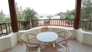 A balcony with a round table and wicker chairs, overlooking a garden and distant buildings. - White Stone Apartment KIMIHURURA (Kigali)
