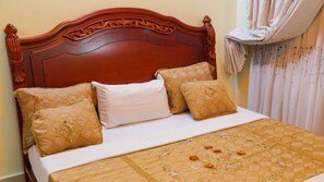 Een bed met een houten hoofdbord, drie kussens en een gewatteerde spreideken.