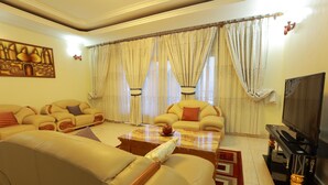 A living room with a sofa set, a coffee table, a television, and curtains. - White Stone Apartment KIMIHURURA (Kigali)