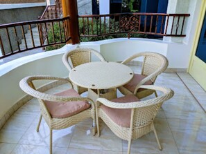 Een ronde rieten tafel met vier stoelen, elk met een kussen, op een betegelde vloer.