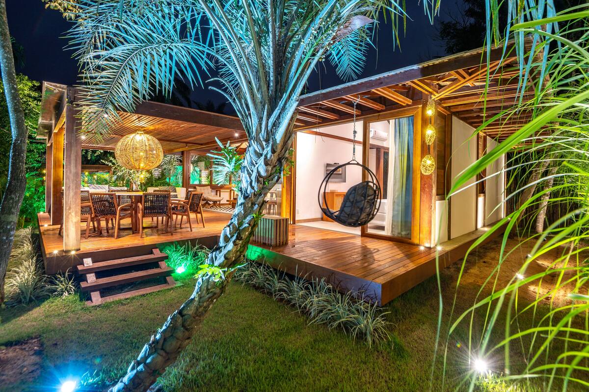 A modern outdoor patio with a hanging chair, wooden deck, and ambient lighting.